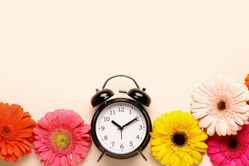Alarm clock and beautiful gerbera flowers on beige background