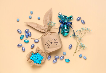 Easter bunny gift bag, candies, chocolate eggs and gypsophila flowers on beige background