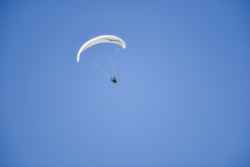 One adult hanging on a white  parachute high in the sky with a clear blue sky as background.