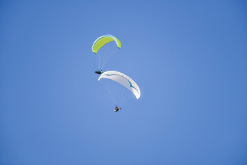 Two adults hanging on a white and green parachute high in the sky with a clear blue sky as background.