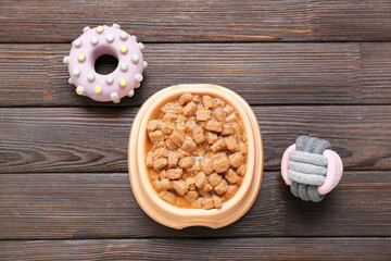 Bowl of wet pet food and toys on wooden background
