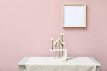 Test tubes with beautiful eustoma flowers on table near color wall