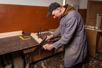 A carpenter works in a workshop with a saw, planer and various tools