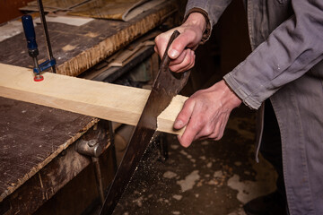 A carpenter works in a workshop with a saw, planer and various tools