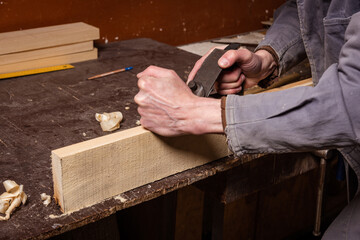 A carpenter works in a workshop with a saw, planer and various tools