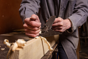 A carpenter works in a workshop with a saw, planer and various tools