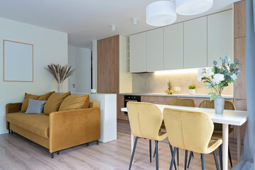 Modern kitchen with living room and dining room with stylish table and chairs. Yellow sofa and...