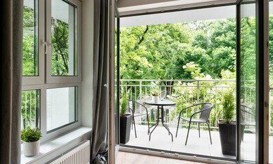Big balcony window in new apartment with beautiful view on green nature and table with chairs. Modern building with patio.	