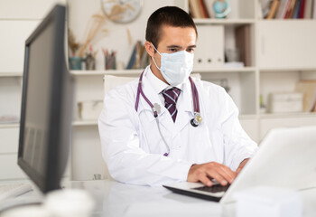 Experienced male therapist wearing surgical mask holding consultation in clinic office - obrazy, fototapety, plakaty