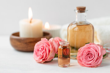 Fototapeta na wymiar Aromatherapy. Concept of pure organic essential rose oil. Elixir with plant based floral or herbal ingredients. Pink flowers extract. Spa atmosphere with candle, towel. White background