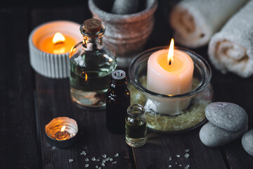 Spa setting with essential oil, candle, sea salt, pebbles, towel on dark wooden background. Massage, aromatherapy. Natural organic ingredients for relaxation, detention. Wellness in salon concept