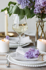 Fototapeta na wymiar Beautiful table decor for a wedding dinner with a spring blooming lilac flowers. Celebration of a special holiday marriage event. Fancy white plates, wineglasses, candles. Countryside style