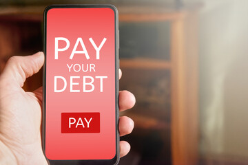 Man holding mobile phone with pay your debt text and pay button on red screen. Online debt payment...