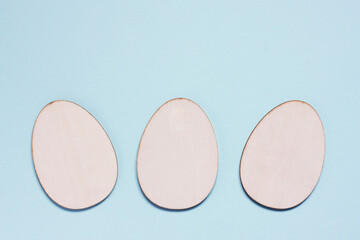 Three flat wooden blanks for creativity in shape of egg on pastel blue background. Happy Easter concept. Mockup for greeting card with space for text. top view, flat lay