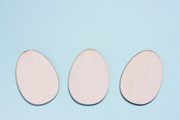 Three flat wooden blanks for creativity in shape of egg on pastel blue background. Happy Easter concept. Mockup for greeting card with space for text. top view, flat lay