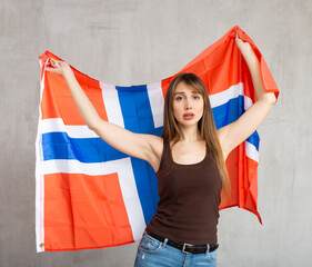 Unhappy young woman in casual clothes waving national flag of Norway while looking at camera at...