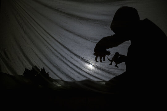 Child play in tent made of blankets and pillows at home. Little Boy play with Dinosaurs in secret place late evening.