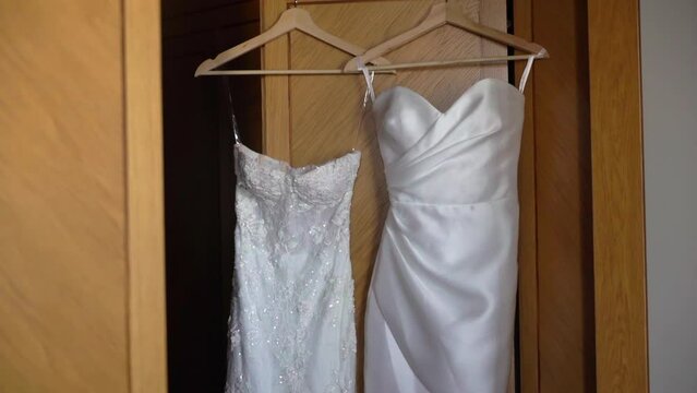 Two beautiful white wedding dress hangs on a hanger on the wardrobe in the bedroom. Morning of the bride, wedding day. Women's fashionable clothes for the holiday.