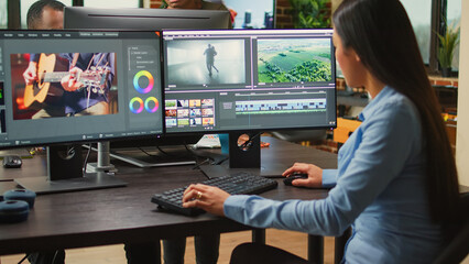 Asian film maker working on movie footage quality with editing software, using multiple monitors in...