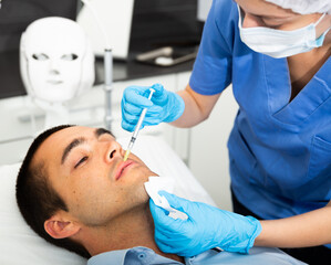 Handsome young man receiving procedure of injection contouring for facial correction in cosmetology clinic .