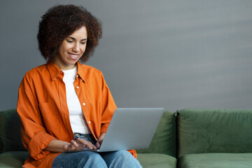 Smiling confident African American woman using laptop computer working online from home. Freelancer...