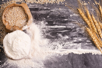 Flour and wheat grains in sacks with wheat ears On a black background table. In a rustic kitchen. Top view.