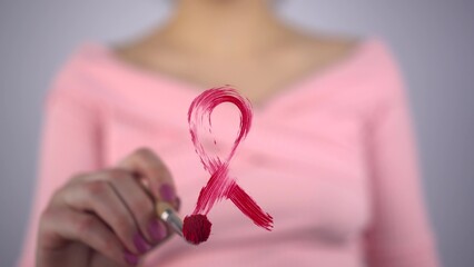 A woman paints a red ribbon on glass in support of cancer patients. Girl draws a symbol of hiv...