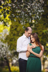 Fototapeta premium Couple in love: young girl in a long green dress and balding man in the garden. Spring or summer love story