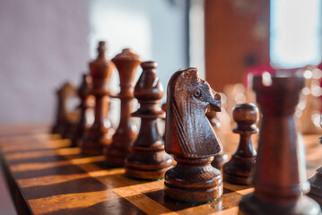 Closeup of wooden brown chess pieces arranged on chessboard over wooden table in hotel room