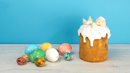 Easter pastries and colored eggs on a blue background. Glazed Easter panettone and colored Easter eggs. - obrazy, fototapety, plakaty