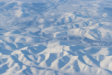 Aerial view of a river in a mountain valley. Winter snowy mountain landscape. Penzhina River, Icheghem Range, Kolyma Mountains. Koryak Okrug (Koryakia), Kamchatka Krai, Siberia, Far East of Russia.