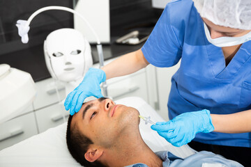 Obraz na płótnie Canvas Portrait of male patient during cosmetology procedure in beauty clinic, getting carbon dioxide injections for face skin rejuvenation