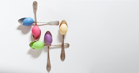 Close-up of colorful Easter eggs in spoons on a white background, copy space