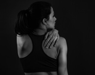 Naklejka premium Beautiful sport woman holding and massage the hand the shoulder and neck on dark background. Black and white. Closeup 