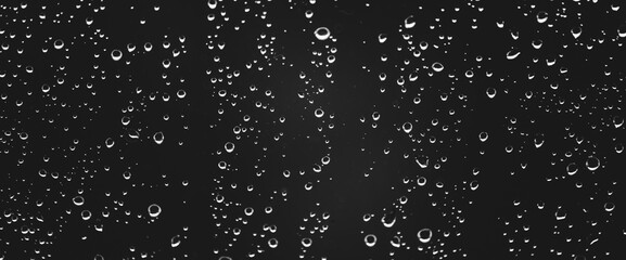 Fototapeta na wymiar Atmospheric minimal grayscale backdrop with rain droplets on glass. Wet window with rainy drops and dirt spots closeup. Blurry minimalist monochrome background of dirty window glass with raindrops.