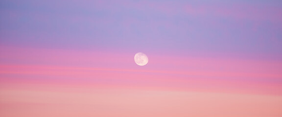 Beautiful backdrop of sunset sky of pink orange lilac colors and moon in center. Colorful smooth dawn sky gradient. Natural background of sunrise. Morning heaven. Slightly cloudy evening atmosphere.