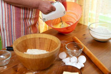 Female hands mixing eggs in bowl by electric mixer in home kitchen. Close-up selective focus.