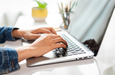 Casual young woman wearing jean shirt, freelance working typing email on laptop at workplace, close up