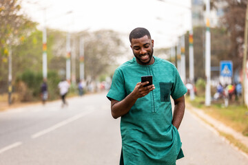 Confident young African man using smartphone outdoors, Tech-savvy individual exploring new apps on phone