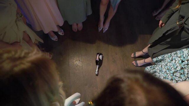 Spin the bottle game. Young women at a party stand in a circle with a bottle spinning in the center.