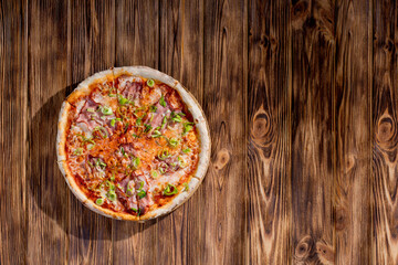 Delicious pizza with mozzarella cheese, ham, leeks on a tomato base on wood background. Copy space