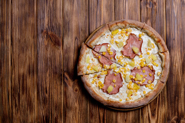 Delicious pizza with ham, pineapple, corn on a creamy base on woden background. Hawaiian pizza