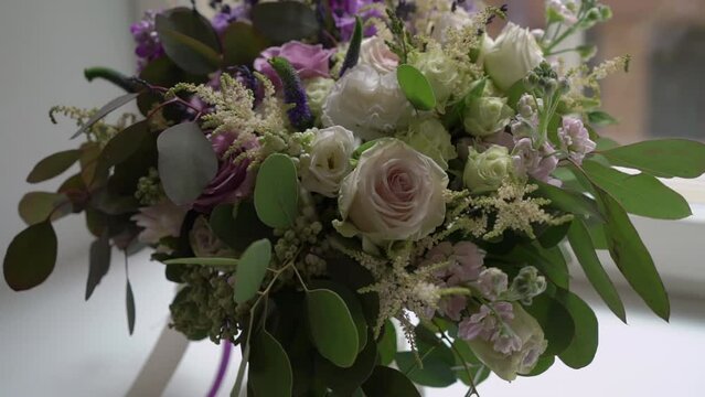 Wedding bouquet of white roses tied with a purple ribbon at windowsill.