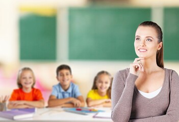 Happy young teacher in class with schoolchild on background.