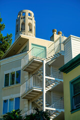 White stucco building facade with exterior stairway entry and large observation tower in afternoon shade san francisco