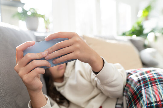 Teenager holding a mobile phone in her hands while at home on the sofa