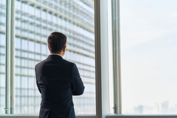 asian businessman standing by window looking at view