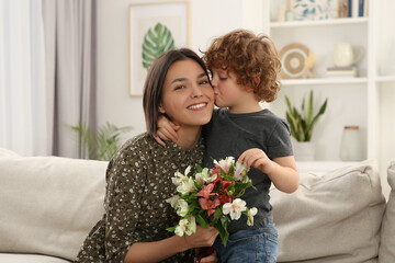 Little son kissing and congratulating his mom with Mother`s day at home. Woman holding bouquet of flowers