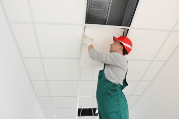 Suspended ceiling installation. Builder working with PVC tile