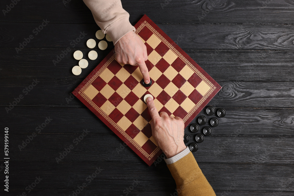 Poster Man playing checkers with partner at black wooden table, top view